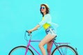 Happy pretty young woman rides a bicycle over colorful blue background