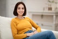 Happy pretty young woman sitting on couch at home Royalty Free Stock Photo