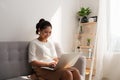 Happy pretty young woman sitting on sofa and using laptop at home Royalty Free Stock Photo