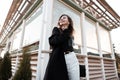 Happy pretty young woman in a trendy black T-shirt in a luxurious long coat in vintage jeans with a cute smile is posing Royalty Free Stock Photo