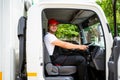 Happy professional truck driver with his assistant wearing a red cap, smiling, looking at the camera from a truck window. Royalty Free Stock Photo