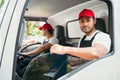Happy professional truck driver with his assistant wearing a red cap, smiling and looking at the camera from a truck window. Royalty Free Stock Photo