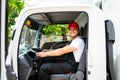 Happy professional truck driver with his assistant wearing a red cap, smiling, looking at the camera from a truck window. Royalty Free Stock Photo