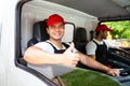 Happy professional truck driver with his assistant wearing a red cap thumb up, smiling, looking at the camera from a truck window Royalty Free Stock Photo