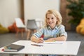 Happy pupil. Joyful school boy smiling away while writing in his notebook, sitting at the desk in classroom Royalty Free Stock Photo