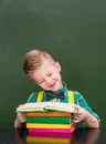 Happy pupil reading a book near empty green chalkboard