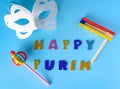 Happy Purim Jewish celebration holiday greeting card.White carnival mask,colorful wooden noisemakers on blue background.