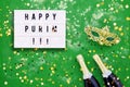 Happy Purim written in light box, two champagne bottles, carnival mask and confetti on green background. Flat lay of Purim