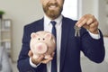 Happy real estate agent or mortgage broker holding piggy bank and keys to new house Royalty Free Stock Photo