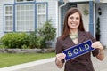 Happy real estate woman holds a sold sign outside a home Royalty Free Stock Photo