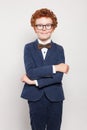 Happy red haired child boy in blue suit standing against white wall background