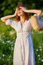 a happy red-haired woman in a light dress stands in a field and covers her face with her hair Royalty Free Stock Photo