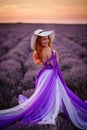 Happy red-haired woman in luxurious dress standing in lavender field at sunset Royalty Free Stock Photo