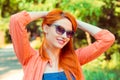 Happy red head woman relaxing hands on head with sunglasses, looking at you camera outdoors park green trees background Royalty Free Stock Photo