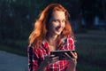 Happy redhair girl with digital tablet in hands posing outdoors, casual modern life