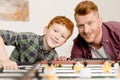 happy redhead father and son smiling at camera while playing table football together at home Royalty Free Stock Photo