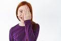 Happy redhead little girl, ginger kid hiding half of face behind hand and laughing, smiling cheerful, standing over