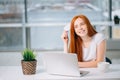 Happy redhead shopper deciding what to buy on line holding a credit card sitting Royalty Free Stock Photo