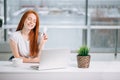 Happy redhead shopper deciding what to buy on line holding a credit card sitting Royalty Free Stock Photo