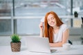 Happy redhead shopper deciding what to buy on line holding a credit card sitting Royalty Free Stock Photo