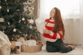 Happy redhead woman in sweater with gifts under Christmas tree with lights. New Year holidays. Christmas