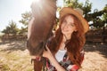 Happy redhead young woman cowgirl with her horse in village Royalty Free Stock Photo