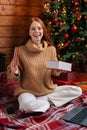 Happy redhead young woman getting Christmas gift box with present on background of xmas tree. Royalty Free Stock Photo