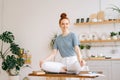 Happy redhead young woman sitting in lotus pose at the desk and looking at camera. Royalty Free Stock Photo