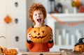 Happy redheaded boy in costume with pumpkin Jack o lantern making scary faces during a Halloween celebration