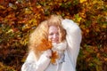 Happy redheaded woman ginger, in her best years with very curly hair in front of colorful autumnal bushes and plays with autumn