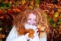 Happy redheaded woman ginger, in her best years with very curly hair stands in front of colorful autumnal red bushes and plays