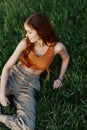 Happy redheaded woman sitting on fresh spring green grass in the garden smiling and looking out into the sun, view from Royalty Free Stock Photo