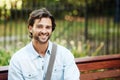 Happy, relax and portrait of a man on a park bench for a break, morning commute or travel. Smile, nature and a young Royalty Free Stock Photo