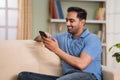 Happy relaxed indian man using mobile phone while sitting on sofa at home during sunday - concept of online dating