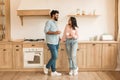 Happy relaxed indian spouses with cups enjoying coffee and free time together in kitchen, full length, free space