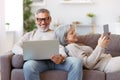 Happy relaxed old retired family couple using modern technologies laptop and digital tablet at home