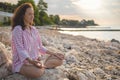 Happy relaxed woman meditation in lotus position practicing yoga sitting on stone beach sea waves Royalty Free Stock Photo