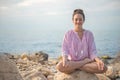 Happy relaxed woman meditation in lotus position practicing yoga sitting on stone beach sea waves Royalty Free Stock Photo