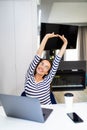 Happy relaxed young woman sitting in her kitchen with a laptop in front of her stretching her arms above her head Royalty Free Stock Photo