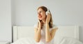 Happy relaxed young woman listening to music with wireless headphones on bed in white room at home Royalty Free Stock Photo