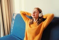 Happy relaxed young woman listening to music with wireless headphones with closed eyes lies on the couch at home Royalty Free Stock Photo