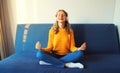 Happy relaxed young woman listening to music with wireless headphones meditating with closed eyes sitting in the lotus position on Royalty Free Stock Photo