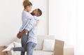 Afro Husband Lifting Wife Standing Among Moving Boxes In Apartment