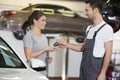 Happy repairman giving car key to woman in workshop Royalty Free Stock Photo