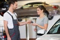 Happy repairman giving car key to woman in workshop Royalty Free Stock Photo