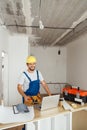 Happy repairman worker in uniform wearing tool belt and hardhat holding hammer and smiling at camera while standing Royalty Free Stock Photo