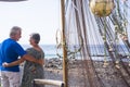 Happy retired lifestyle with couple of senior people hug and look eachother viewed from back - ocean and beach in background -