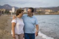 Happy retired mature couple walking on the beach - pensioner woman and her husband taking romantic walk together enjoying sweet Royalty Free Stock Photo