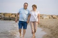 Happy retired mature couple walking on the beach - pensioner woman and her husband taking romantic walk together enjoying sweet Royalty Free Stock Photo