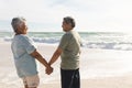 Happy retired multiracial senior couple holding hands while looking at each other on sunny beach Royalty Free Stock Photo